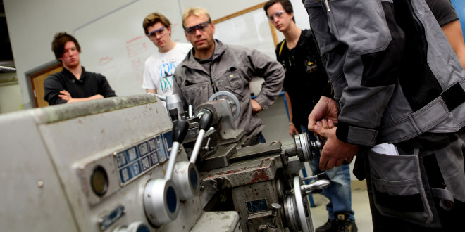 Lærer og tre elever som ser på at en fjerde elev skrur på en maskin